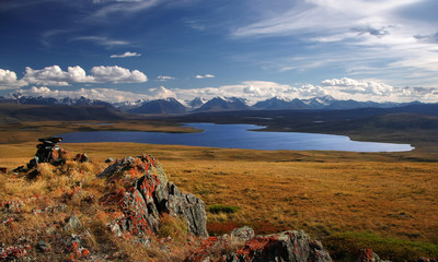 Clean mountain lake on the background of snow covered mountains and glaciers rocks  with red lichen...