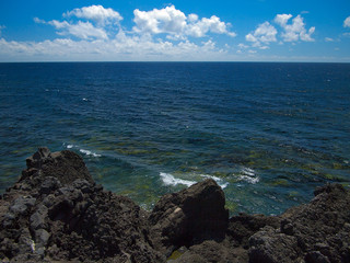 Ocean waves breaking on the rocky coast of hardened lava with caverns and cavities. Deep blue sky with white clouds on the horizon. Lanzarote, Canary Islands, Spain