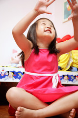 Young girl sitting cross-legged, looking up, hands raised