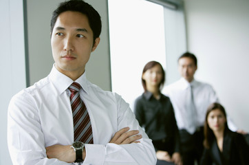 Businessman standing with arms crossed, looking away, people in the background