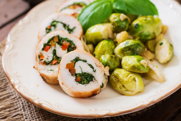 Chicken rolls with greens, garnished with stewed Brussels sprouts, apples and leeks on plate.