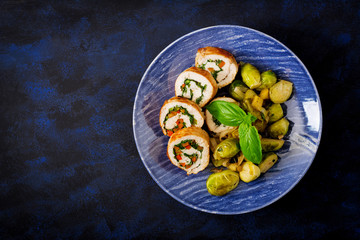 Chicken rolls with greens, garnished with stewed Brussels sprouts, apples and leeks on a blue plate. Top view