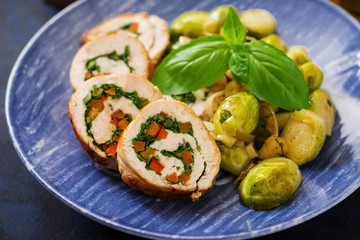 Chicken rolls with greens, garnished with stewed Brussels sprouts, apples and leeks on a blue plate.