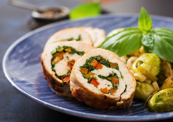 Chicken rolls with greens, garnished with stewed Brussels sprouts, apples and leeks on a blue plate.