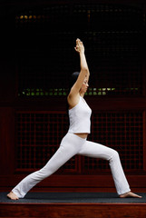 Woman stretching with both arms raised together above head, doing yoga pose, side shot