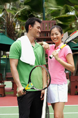Man and women standing on tennis court with tennis rackets