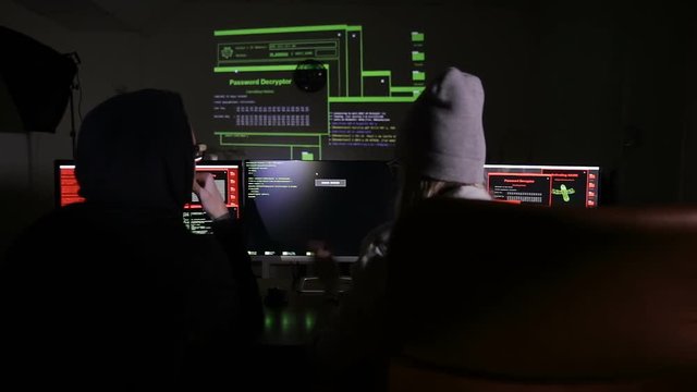 Male and female hackers working on computers with data code on display screens in a dark room. HD.