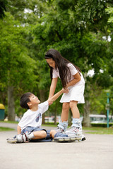 Children rollerblading, boy on the ground, girl pulling him up