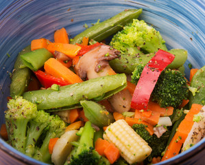 Closeup of healthy steamed vegetables in a blue bowl, with herbs