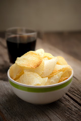 potato chips in bowl with cola on wooden table background.