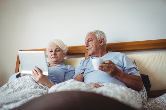 Senior woman using digital tablet and man having cup of coffee