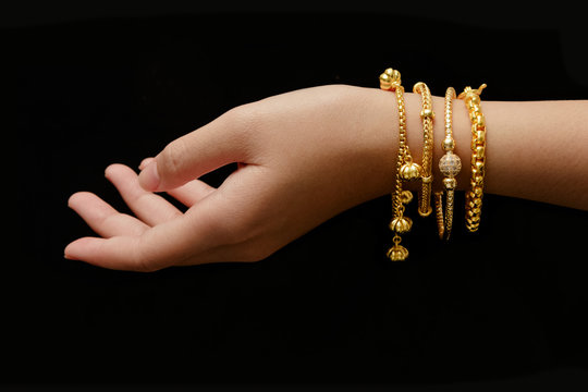 woman's hand with many different golden bracelets on black backg