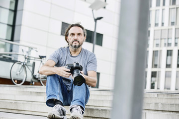 Fotograf sitzt mit seiner Kamera auf einer Treppe