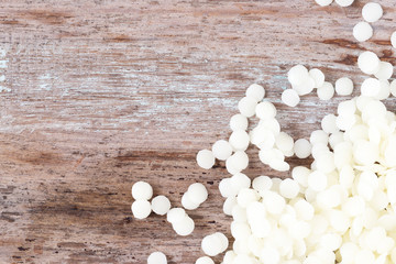 white cosmetic beeswax pellets on wooden background.
