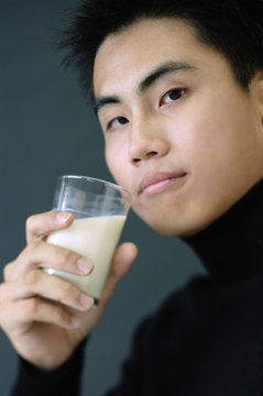 Young man holding glass of milk, looking at camera