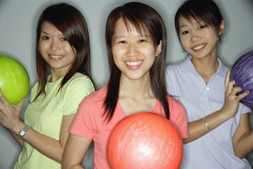 Three young women holding bowling balls, smiling at camera