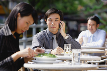 Business people at outdoor cafe, focus on man with mobile phone