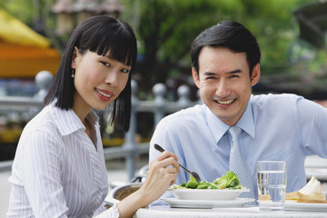 Businesswoman and businessman at outdoor cafe, smiling at camera