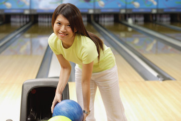 Woman selecting bowling ball, smiling at camera
