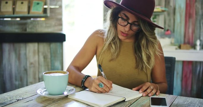 Woman writing in journal in cafe, working in mobile office
