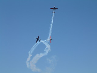 4 small propeller plane in aerobatic display with smoke trails behind them