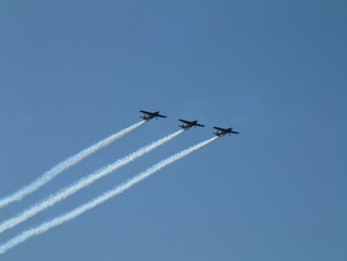 4 small propeller plane in aerobatic display with smoke trails behind them