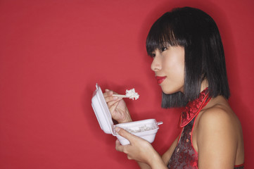 Woman against red background, eating rice from a Styrofoam container