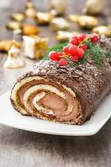 Chocolate yule log cake with red currant on wooden background
