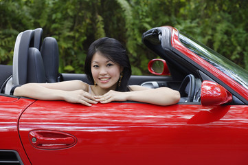 Woman sitting in red sports car, smiling at camera, portrait