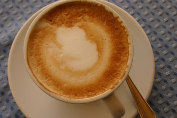 Cappuccino in weisser Tasse auf blauem Tischtuch in ansicht von oben