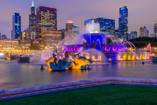 Chicago skyline panorama with skyscrapers and Buckingham fountain in Grant Park at night lit by colorful lights.