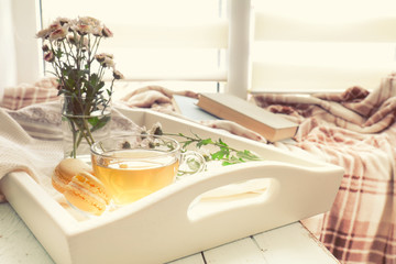 Cup of tea, books, chrysanthemum flowers and macaroons in tray on the table. Cozy home concept. Coloring and processing photo in vintage style.