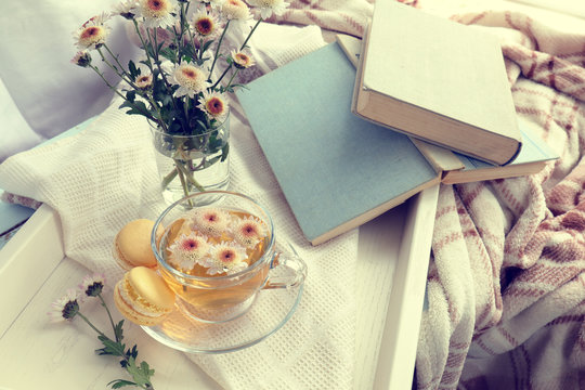 Cup of tea, books, chrysanthemum flowers and macaroons in tray on the table. Cozy home concept. Coloring and processing photo in vintage style.