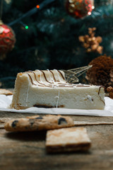 Beautiful homemade cake cheesecake on a white paper on the wooden background. Next chocolate chip cookies, Christmas gifts, Christmas tree, cones and toys. Conceived to celebrate the new year.