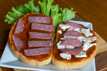 Slice of bread with chutney and feta cheese and salami on wooden background