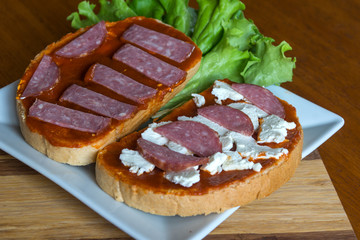 Slice of bread with chutney and feta cheese and salami on wooden background