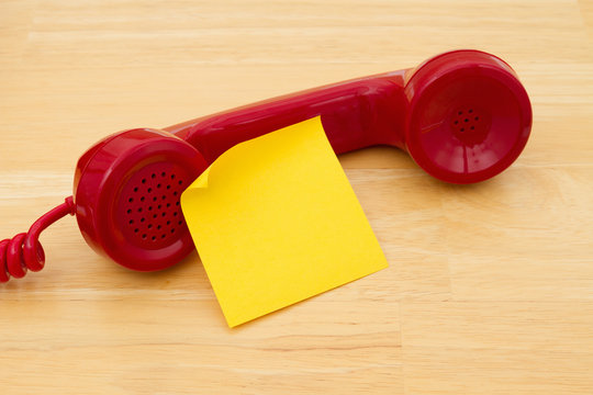 A retro red phone with yellow sticky note