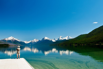 Man looking at the majestic snow-capped mountains reflecting in the calm waters of Lake McDonald in...