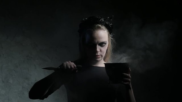 Dark portrait of evil witch with knife and bowl. 4K UHD