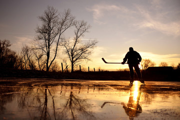 Young hockey player on natural ice during calm winter sunset - obrazy, fototapety, plakaty