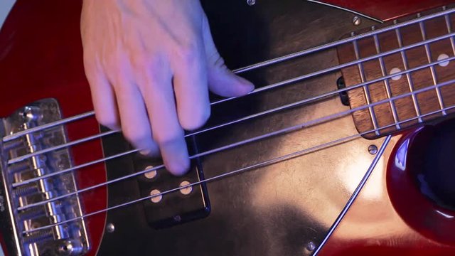 Musician playing five string electric bass guitar; close up on right hand, guitar body and strings; 
