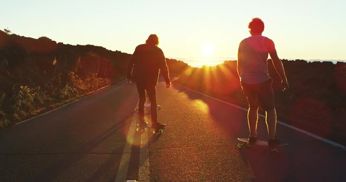 Skateboarders riding down mountain road into the sunset