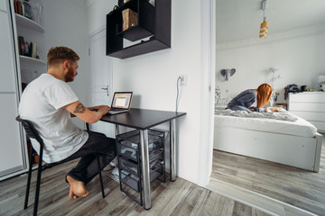 Dad works at laptop, mom and baby on the bed