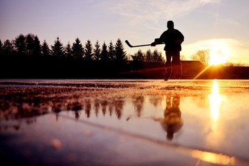 Reflexion of young hockey player on bright natural ice during colorful calm winter sunset on january frozen lake