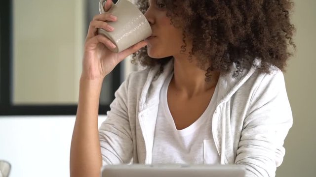 Mixed-race woman at home using tablet and drinking tea