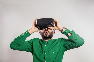 Young emotional middle eastern excited man with beard and green shirt using a VR headset and experiencing virtual reality.