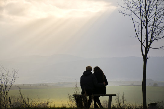 Loving couple silhouette on the bench over wonderful spring landscape with glory sky full of sun beams
