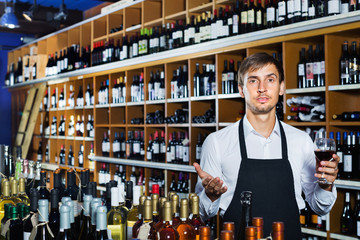 Seller man wearing apron suggesting to try glass of wine