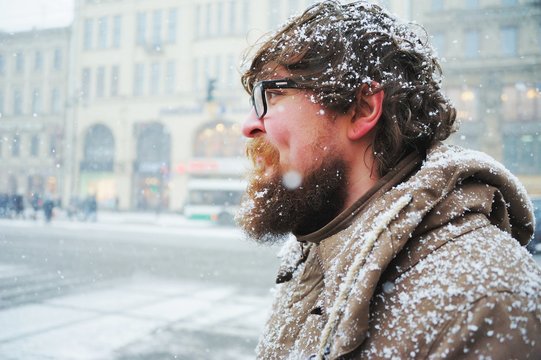 Reckless Russian bearded guy in glasses without a hat, covered with snow, walking in the center of St. Petersburg during a Blizzard on a cold winter day