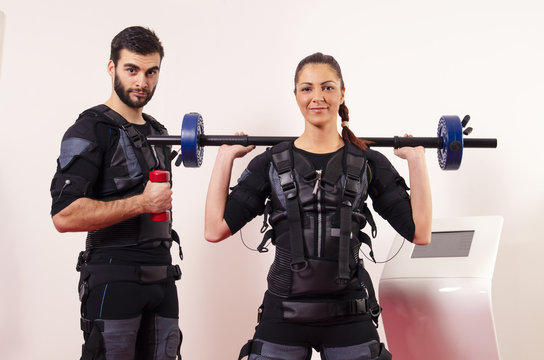 Male and female posing with weights next to ems machine